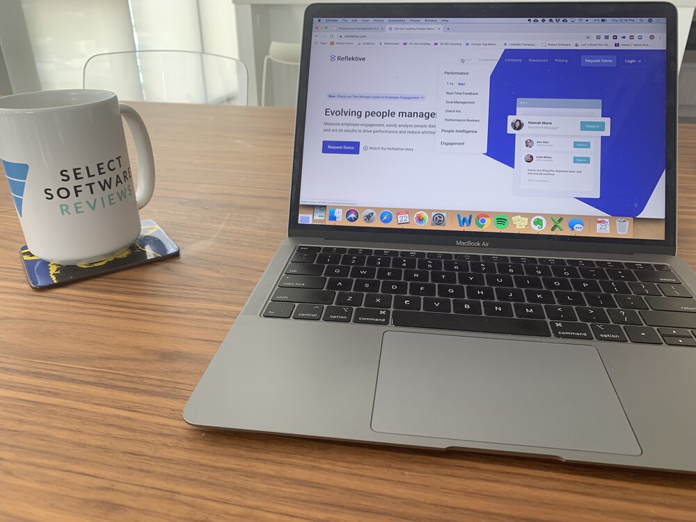 Viewer enjoying coffee in a SelectSoftware Reviews mug and looking at Reflektive software demo screen on computer