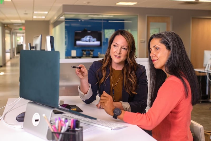 Two women working hard together at a computer finding words of appreciation for employees