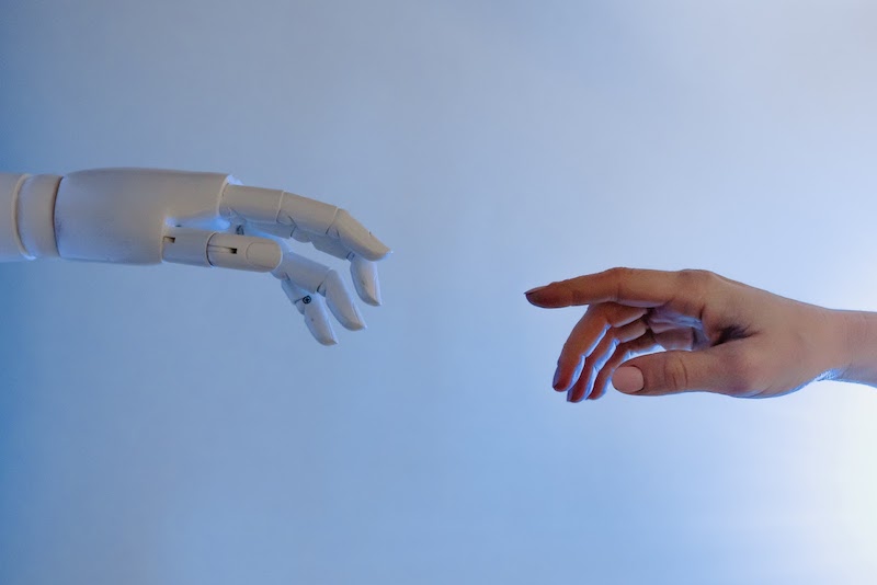 The hand of an AI robot reaching toward a human hand