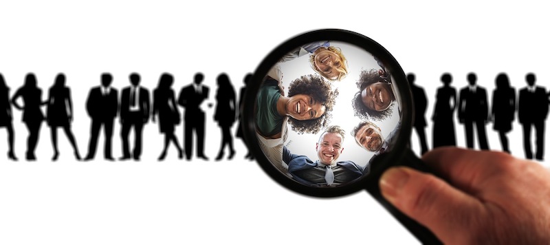 A hand looking at happy customers through a magnifying glass