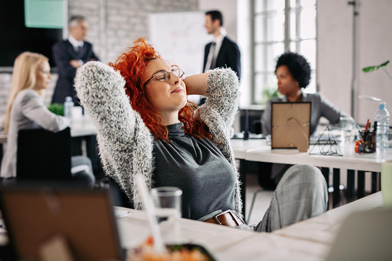 An HR professional, smiling and leaning back in their chair with hands behind their head, enjoys a break thanks to automating tedious manual HR tasks.