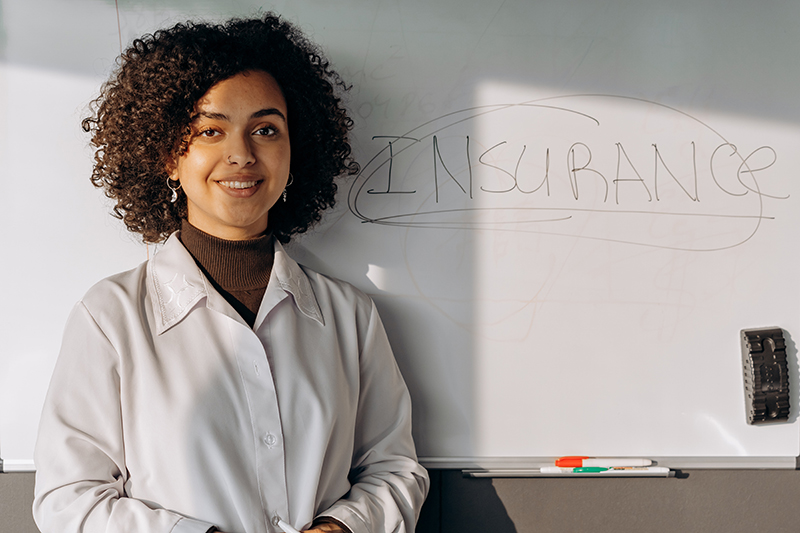 An HR professional standing in front of a whiteboard that has the word insurance written on it.