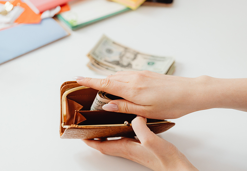 An employee’s hand saving part of their earned income by placing it in a wallet as part of a financial wellness plan.