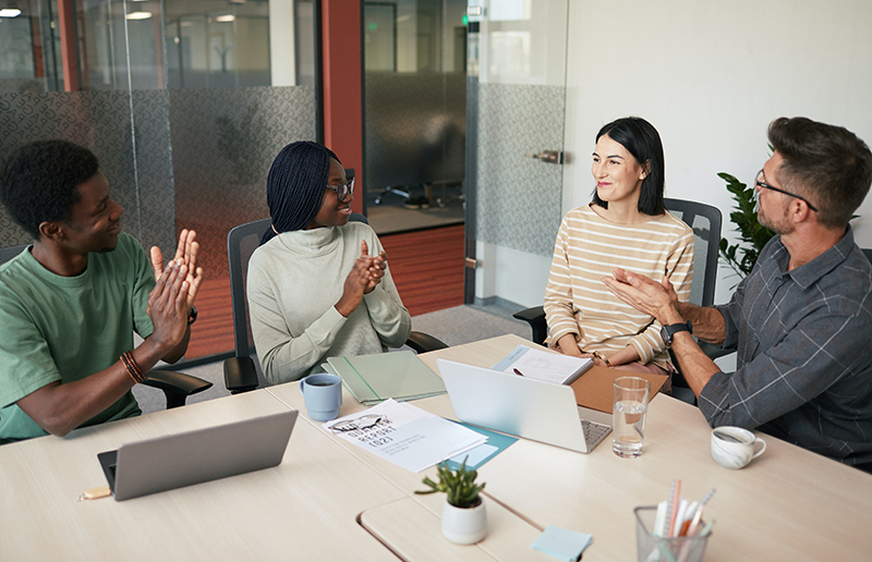 An employee receives praise from colleagues at a work meeting because they are able to perform well thanks to the guidance offered by a financial wellness program.
