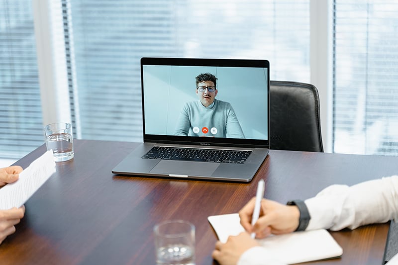 A laptop shows a remote employee attending a virtual performance management meeting with their manager.