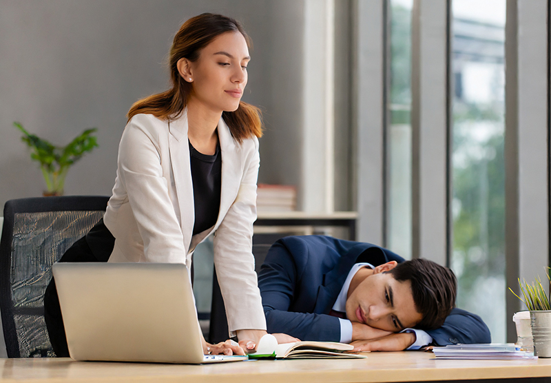 A high-performing employee who is busy next to a lazy employee who is sleeping.