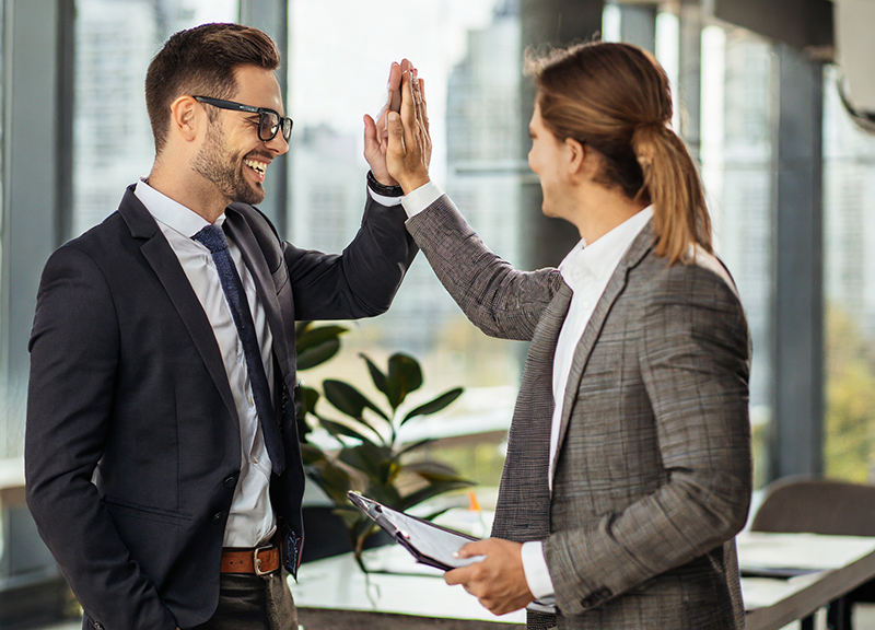 A male and female colleague high-five each other in a display of peer-to-peer in the office.