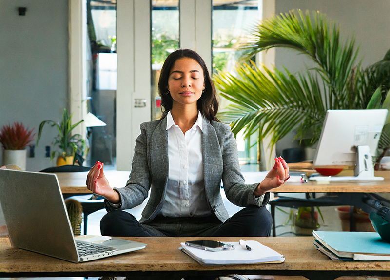 A professional woman meditating at her desk to restore her mental health after dealing with toxic leadership.