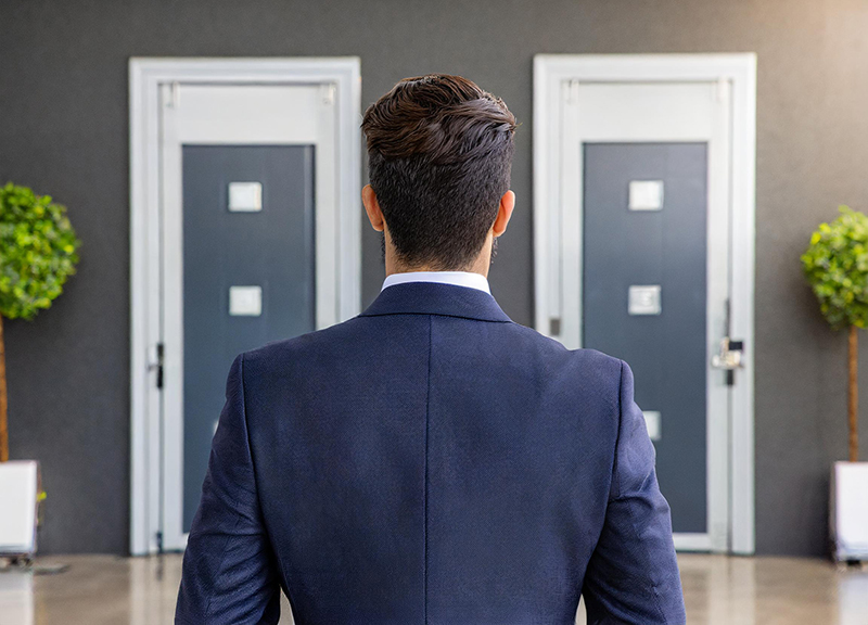 A professionally dressed man standing in front of doors representing his career options via an outplacement service. 